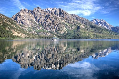 A serene lake reflects majestic mountains under a clear blue sky, with a small boat gently floating on the water.