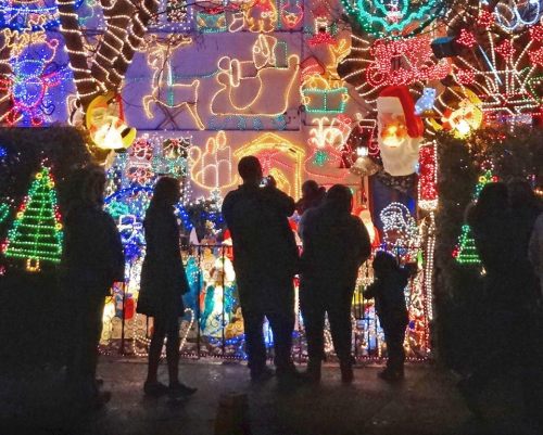 A group of people silhouetted against a colorful display of Christmas lights and decorations.