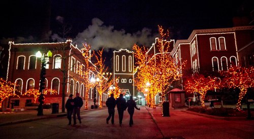 A nighttime street scene with buildings and trees adorned with bright orange lights, creating a festive atmosphere.