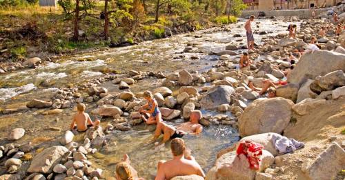 People enjoying a sunny day by a rocky river, some swimming and relaxing in the water.