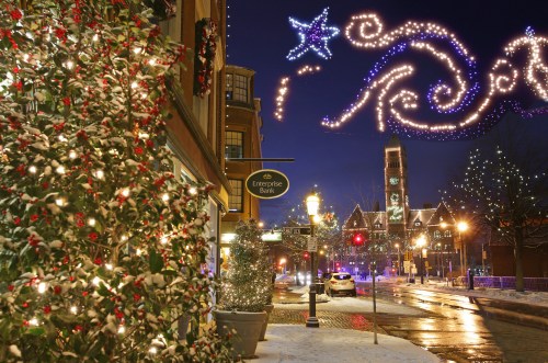 A festive street scene with holiday lights, snow-covered trees, and a charming building in the background at night.