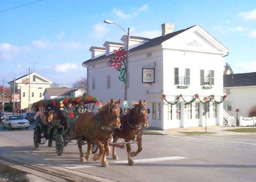 A horse-drawn carriage decorated for the holidays passes by a festive building in a small town.