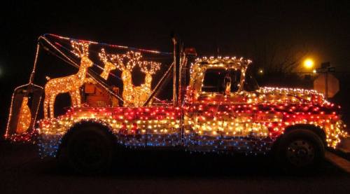 A decorated truck covered in colorful Christmas lights, featuring illuminated reindeer in the back.