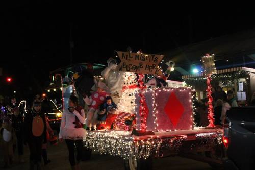 A festive parade float decorated with lights, stuffed animals, and a sign reading "All Misfits Welcome Here."
