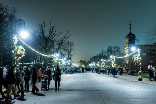 A festive street at night, lined with holiday lights and decorations, with people walking and enjoying the atmosphere.