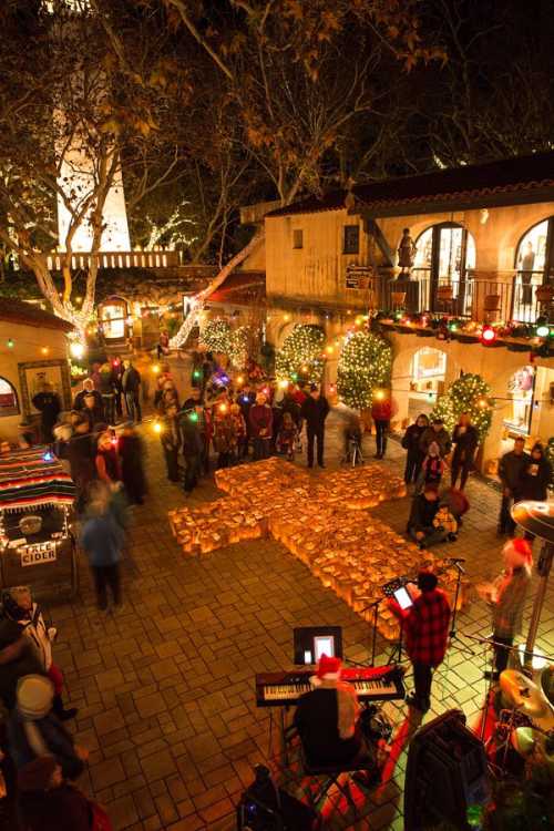 A festive outdoor scene with people celebrating, decorated with lights and a large gingerbread man made of cookies.