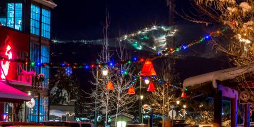 A festive night scene with colorful lights, snow-covered trees, and a ski slope illuminated in the background.