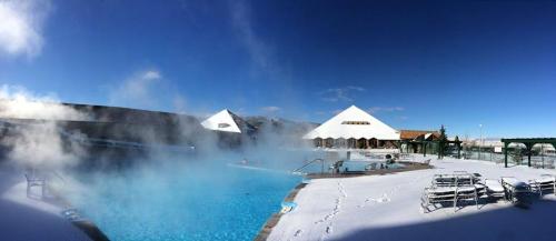 A panoramic view of a steaming outdoor pool surrounded by snow, with a clear blue sky and mountains in the background.