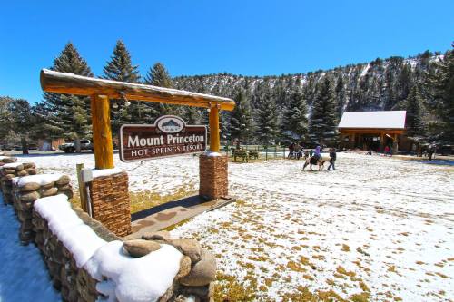 Sign for Mount Princeton Hot Springs Resort, surrounded by snow-covered ground and pine trees under a clear blue sky.
