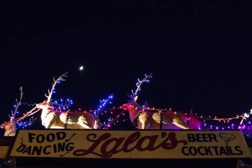 A festive sign for "Lala's" with illuminated reindeer and colorful lights against a night sky with a crescent moon.