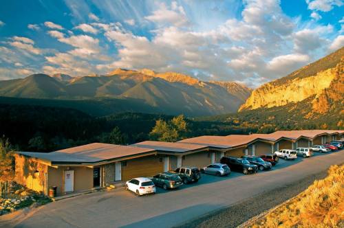 A scenic view of a mountain range with a row of buildings and parked cars in the foreground under a colorful sky.