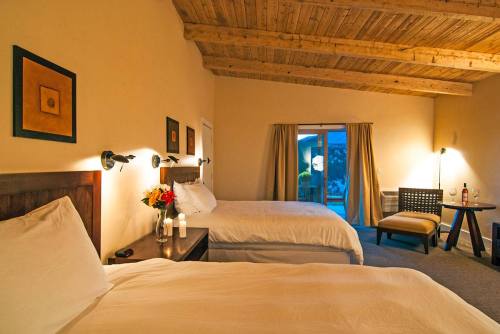 Cozy hotel room with two beds, wooden beams, and a patio door leading to an outdoor area. Decorated with flowers and art.