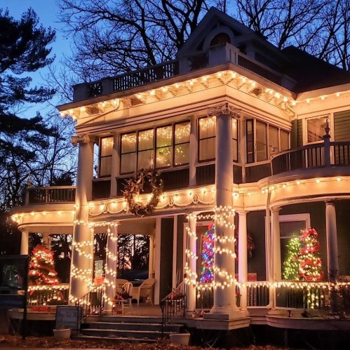 A beautifully decorated house with festive lights and Christmas trees, set against a twilight sky.