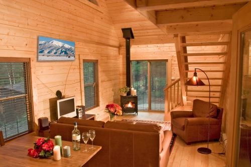 Cozy wooden cabin interior with a fireplace, seating area, and a staircase, featuring warm lighting and decorative elements.