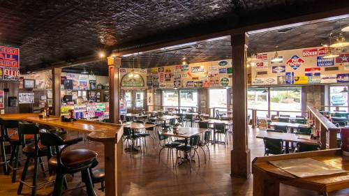 Interior of a rustic restaurant with wooden tables, chairs, and walls adorned with various vintage signs.