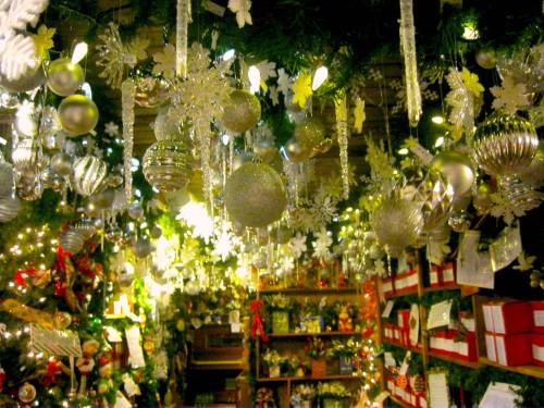 A festive display of silver ornaments and decorations hanging from greenery, with twinkling lights and gift boxes below.