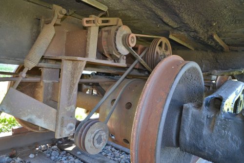 Close-up of rusty train undercarriage components, including pulleys and belts, on a gravel track.