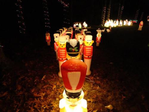 A row of illuminated toy soldiers in a dark outdoor setting, surrounded by festive lights and decorations.