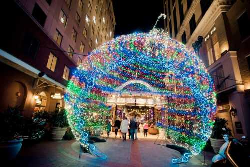 A colorful, illuminated archway made of lights welcomes visitors to a festive outdoor area at night.