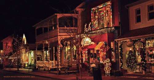 A festive street scene at night, adorned with colorful holiday lights and decorations on charming storefronts.