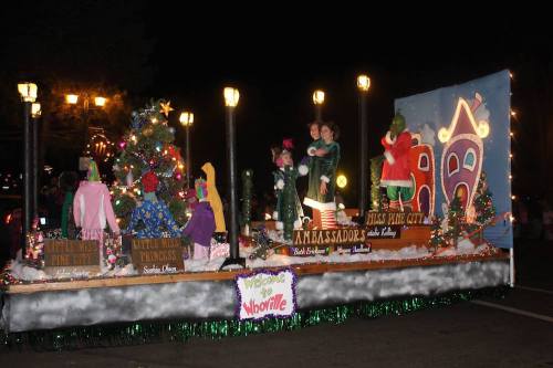 A festive parade float decorated with a Christmas tree, lights, and characters celebrating the holiday season.