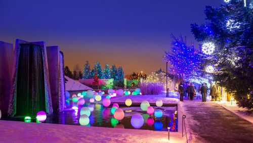 A winter scene with colorful lights, a waterfall, and glowing orbs reflecting in a snowy landscape.