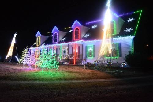 A brightly lit house decorated with colorful Christmas lights and festive displays, set against a dark night sky.