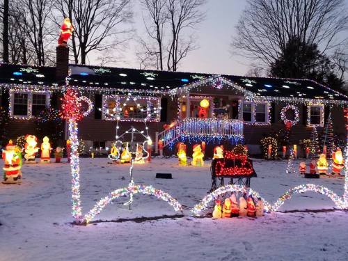 A house decorated with colorful Christmas lights and festive figures, surrounded by snow at dusk.