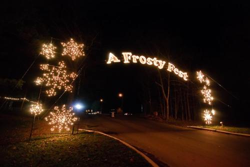 A festive archway reading "A Frosty Fest" illuminated by lights, surrounded by snowflake decorations at night.