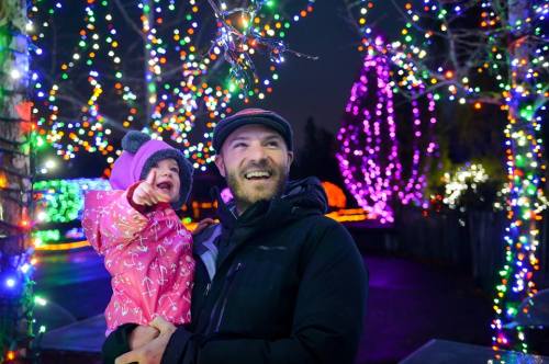 A man holds a smiling child in a colorful, illuminated outdoor setting filled with festive lights.