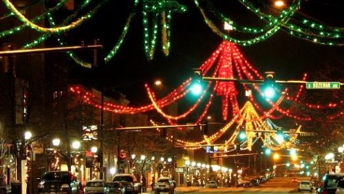 Colorful holiday lights adorn a city street at night, creating a festive atmosphere with green and red decorations.