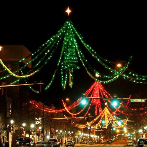 Colorful Christmas lights in a festive display, with green and red decorations illuminating a city street at night.
