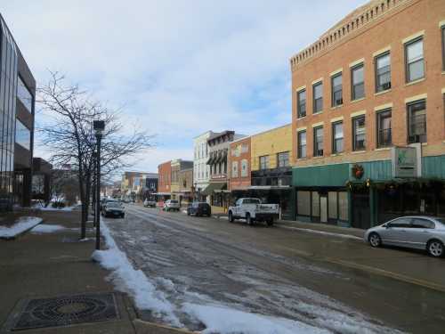 A quiet street lined with brick buildings, some decorated for the holidays, and a light dusting of snow on the ground.