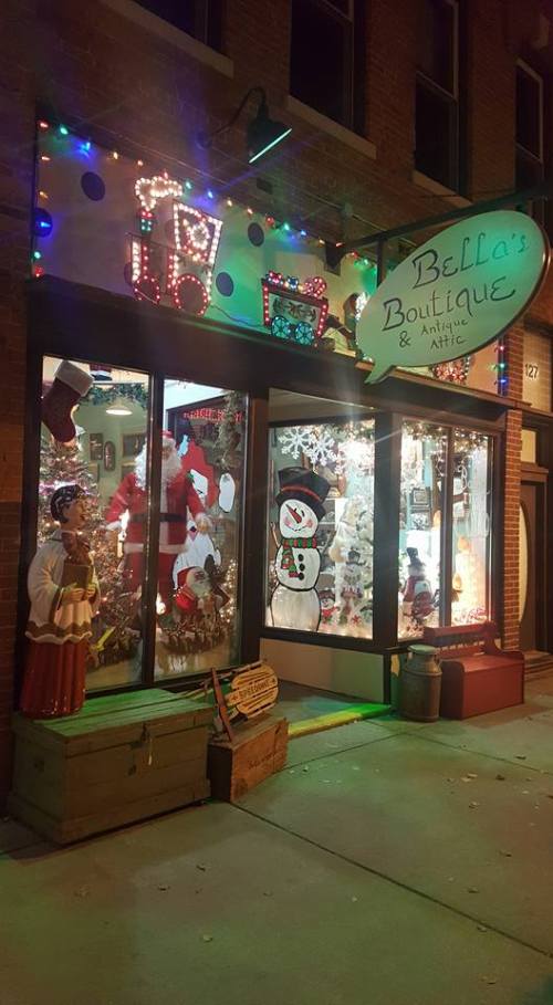A festive boutique window decorated with holiday lights, a snowman, and a Christmas tree, showcasing seasonal decor.