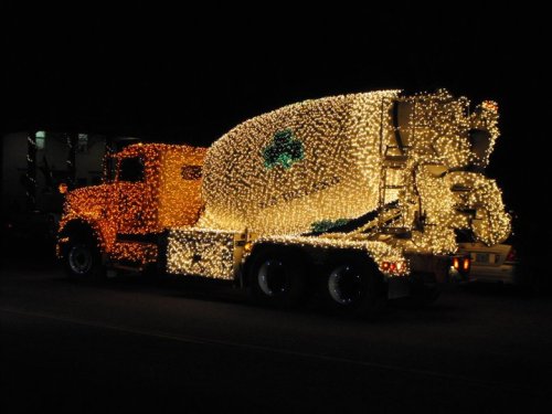 A brightly lit cement truck adorned with colorful holiday lights, parked on a dark street at night.