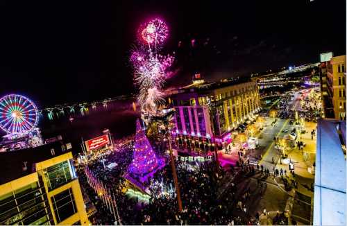 A vibrant night scene of a festive celebration with fireworks, a large Christmas tree, and a bustling crowd by the waterfront.