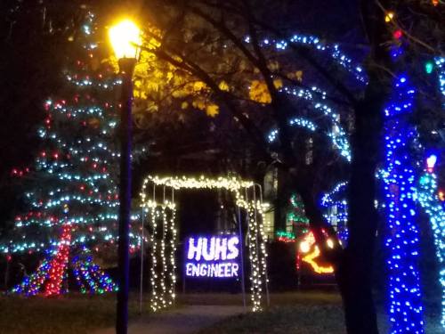 Colorful holiday lights decorate trees and an archway, with a sign reading "HUHS ENGINEER" illuminated at night.