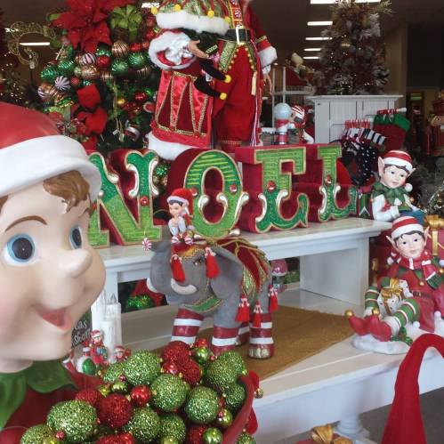 A festive display featuring a large "NOEL" sign, holiday decorations, and cheerful elf figurines.