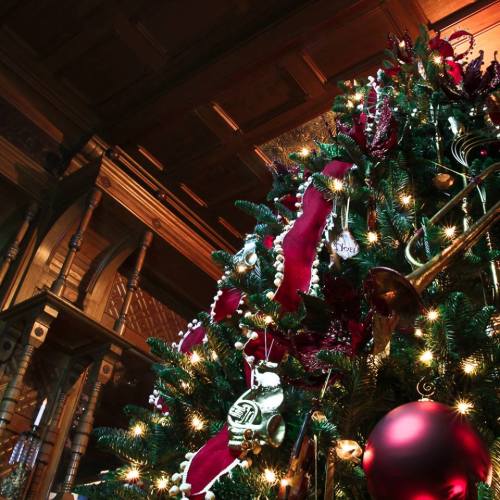 A beautifully decorated Christmas tree with red and gold ornaments in a warmly lit, elegant interior.