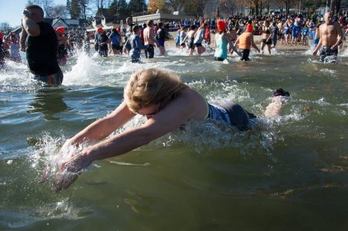 A person dives into a chilly lake surrounded by a crowd of people enjoying a winter swim event.