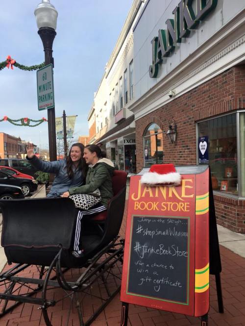 Two women take a selfie in a festive sleigh outside Janke Book Store, decorated for the holiday season.