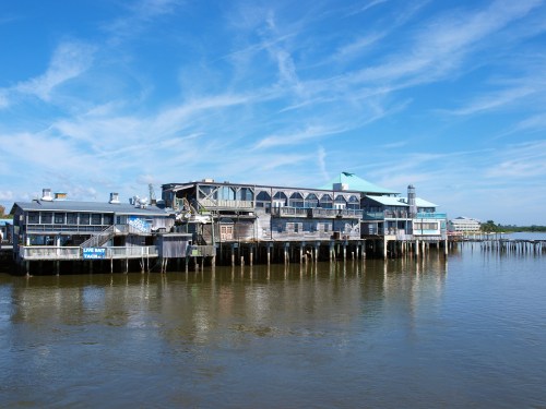 A waterfront building with multiple levels, featuring large windows and a blue sky with wispy clouds above.