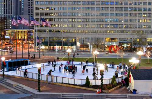 A bustling ice skating rink in a city square, surrounded by flags and festive lights, with skaters enjoying the evening.