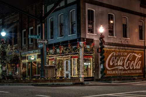 A festive street corner at night, adorned with holiday lights and a vintage Coca-Cola advertisement on the building.