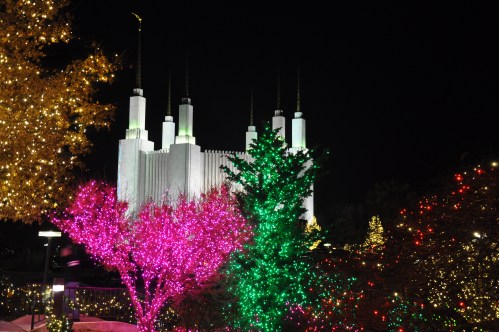 A brightly lit scene featuring colorful trees and a large, illuminated building at night.