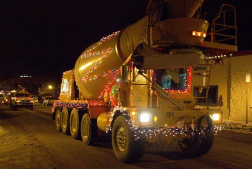 A brightly lit cement mixer truck decorated with colorful Christmas lights driving down a street at night.