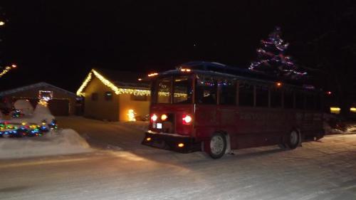 A red bus drives through a snowy street adorned with colorful holiday lights at night.