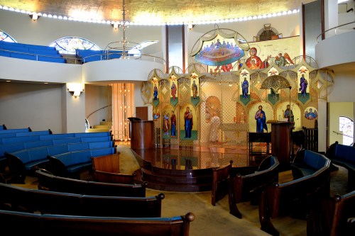 Interior of a church featuring ornate icons, wooden pews, and a bright, spacious altar area.