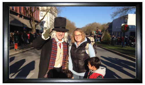 A man in a top hat and vintage attire poses with a woman in a vest, surrounded by a festive street scene.