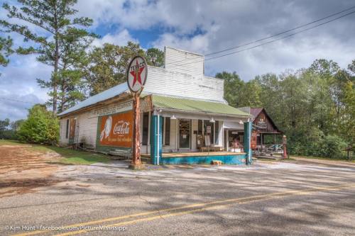 A vintage store with a Coca-Cola sign, surrounded by trees and a cloudy sky, along a rural road.